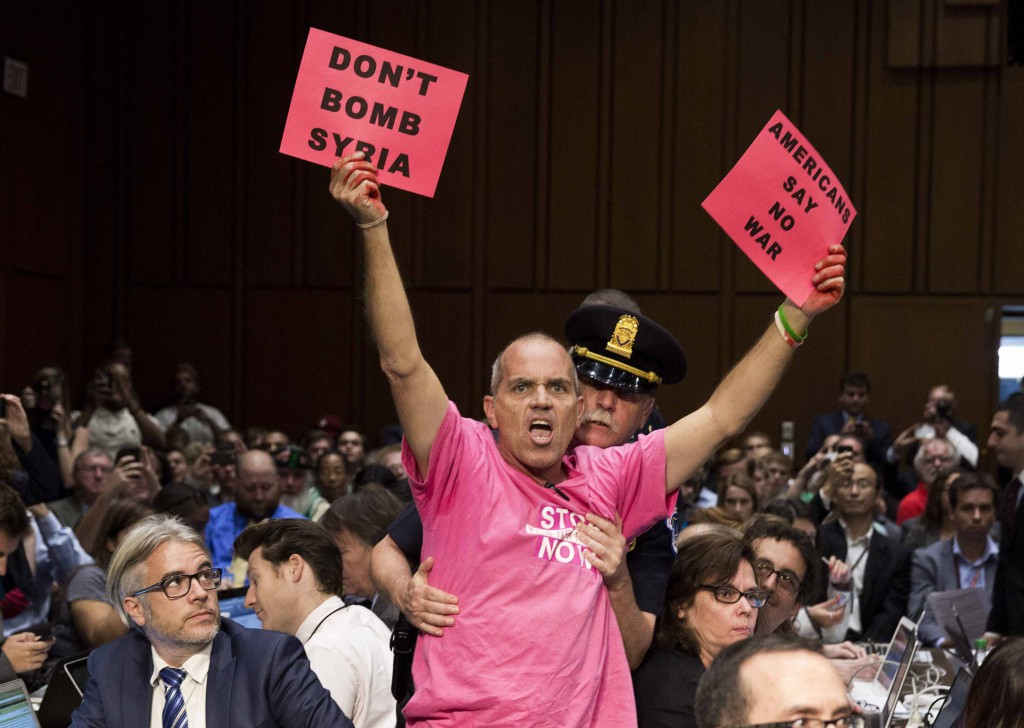 A protester waves signs as Obama administration officials arrive to present the case for U.S. military action against Syria on  Sept. 3 to a Senate Foreign Relations Committee hearing on Capitol Hill in Washington. PHOTO: CNS/Joshua Roberts, Reuters