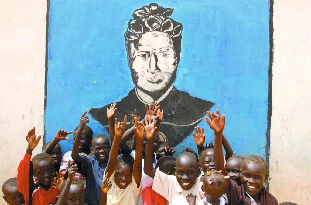 Children raise their hands in front of a mural of St. Josephine Bakhita, an African slave and victim of violence, who died in 1947. PHOTO: CNS/Andrew Heavens, Reuters