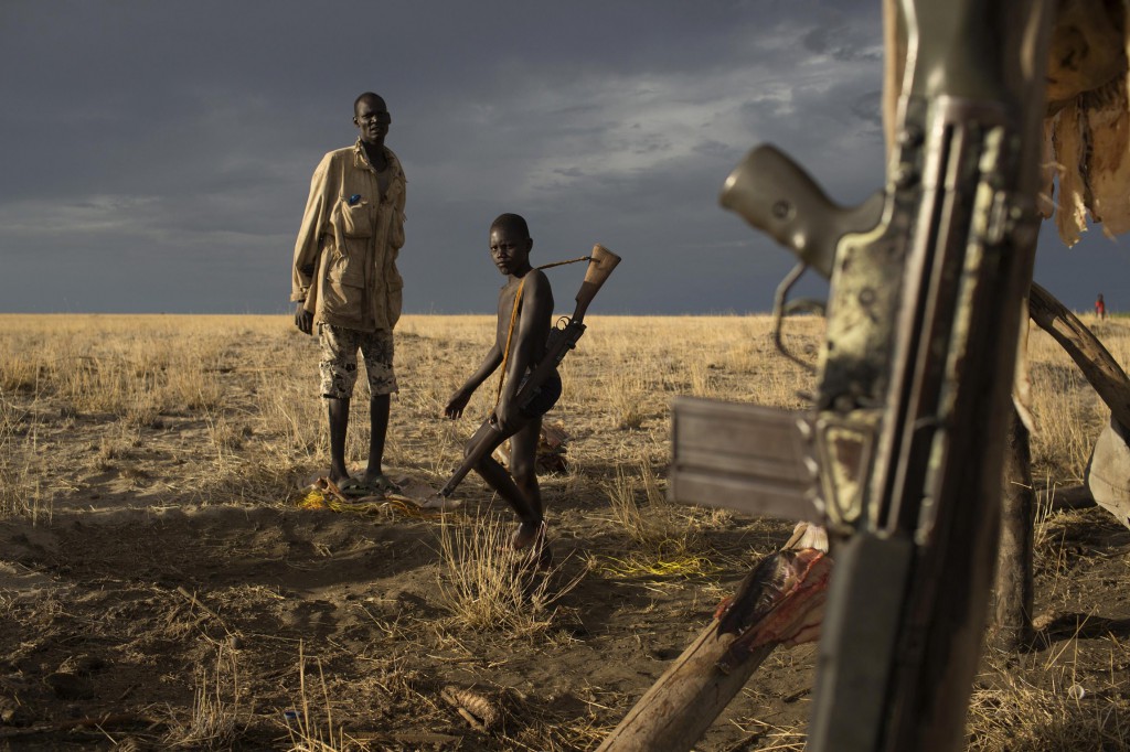 A Turkana man and a boy carrying a gun look on in early October as a G3 battle rifle hangs from a structure  used to dry fish at a fishing camp on the shores of Lake Turkana in northwestern Kenya. Catholic church leaders have undertaken initiatives to reduce violence between the Turkana and Pokot communities skirmishing over land and natural resources in recent months, fueled in part by the discovery of oil in the region. PHOTO: CNS/Siegfried Modola, Reuters