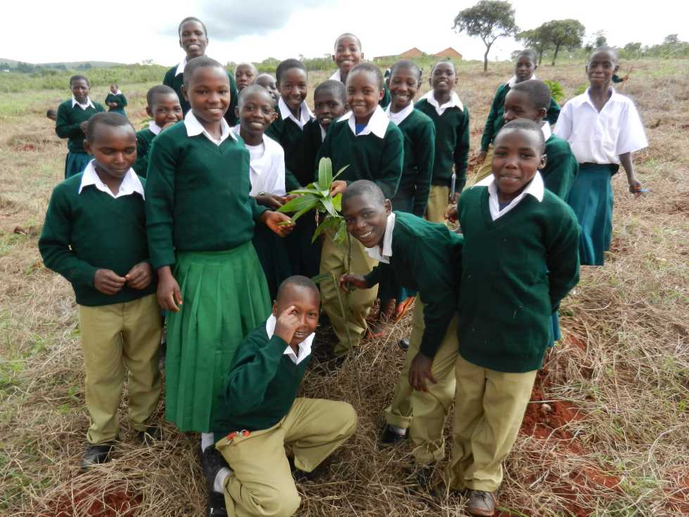 Students at Njelela Environmental Secondary School (NESS) proudly show off a new mango plant in a field near the school. Many of the children spend hours before and after school in the fields, planting a variety of crops. 