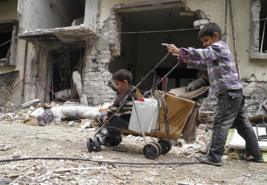 A boy pushes a stroller holding water and another child past destroyed buildings in the besieged area of Homs, Syria, Feb. 2. Syrians fleeing to neighboring Jordan from Homs said some people there are starving to death for lack of food. PHOTO: CNS/Thaer Al Khalidiya, Reuters