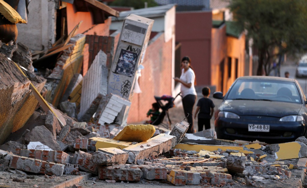 A woman walks with children amid debris around a home April 3 following an earthquake and tsunami that hit the northern port of Iquique, Chile, April 2. The natural disaster did damage, triggered tsunami warnings and claimed at least six lives, but has been much less destructive than previous earthquakes in the region. PHOTO: CNS/Ivan Alvarado, Reuters