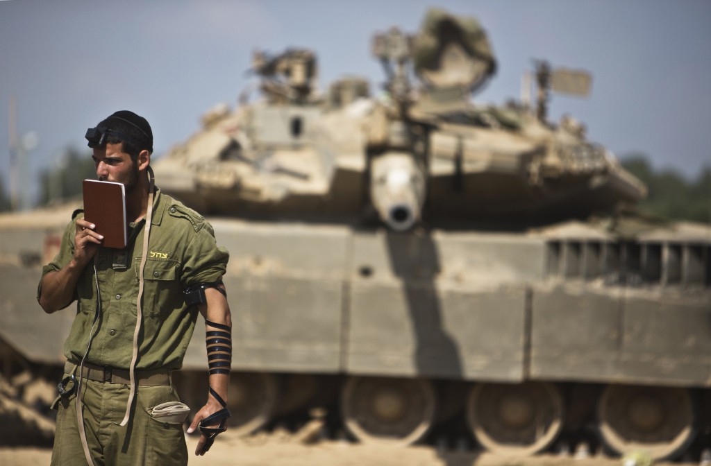 An Israeli soldier prays in front of a tank at a military staging area near the border with the Gaza Strip July 24. Fighting pushed the Palestinian death toll over 700. PHOTO: CNS/Nir Elias, Reuters