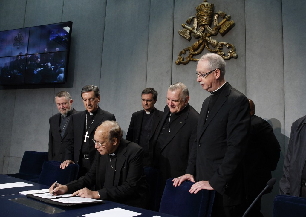 Cardinal Oswald Gracias of Mumbai, India, signs a document at a Vatican news conference on 26 October in which leaders of the world's regional bishops conferences appealed for action on climate change. From left behind the cardinal are Auxiliary Bishop Jean Kockerols of Mechelen-Brussels, Belgium; Cardinal Ruben Salazar Gomez of Bogota, Colombia; unidentified priest; Archbishop Thomas G Wenski of Miami; and Archbishop Richard Smith of Edmonton, Alberta. Photo: CNS