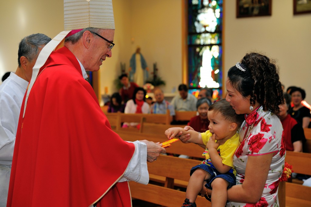 Auxiliary Bishop Don Sproxton participates in the Chinese New Year custom of giving red packets to children during the Thanksgiving Mass at Holy Family Catholic Church in Como. Photo: Supplied