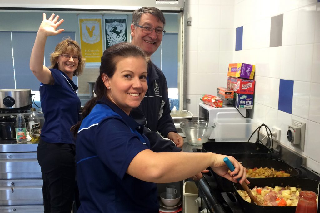 St Gerard’s Primary School staff Allison Burgess and Juscinta Staley, with Principal Mark Miloro, are all smiles as they cook meals for poor, disadvantaged and homeless people on May 31. Photo: Supplied