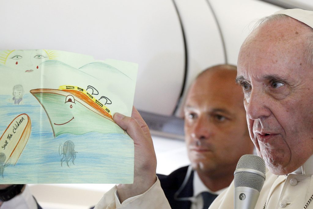 Pope Francis shows a drawing given by a child in a refugee camp as he answers questions from journalists aboard his 16 April flight from the Greek island of Lesbos to Rome. Journalists must not foment fear when covering issues or events such as forced migration due to war or famine, the Pope said during a 22 September audience with representatives of Italy's National Association of Journalists. Photo: CNS/Paul Haring