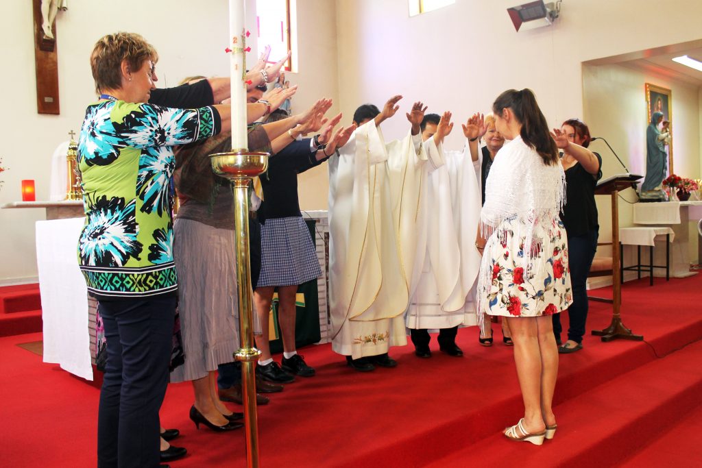 Teacher at St Joseph’s School in Northam, Rebecca Doughty, receives a blessing from Fathers George James and Simeon San, her fellow staff members and student Shari Dimasi after being welcomed into the Catholic Church. Photo: Supplied