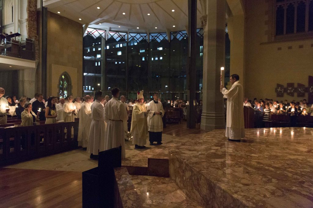 Deacon Paul Russell holds the candle on the sanctuary during the Easter Vigil Mass on Saturday 15 April. Photo: Ron Tan
