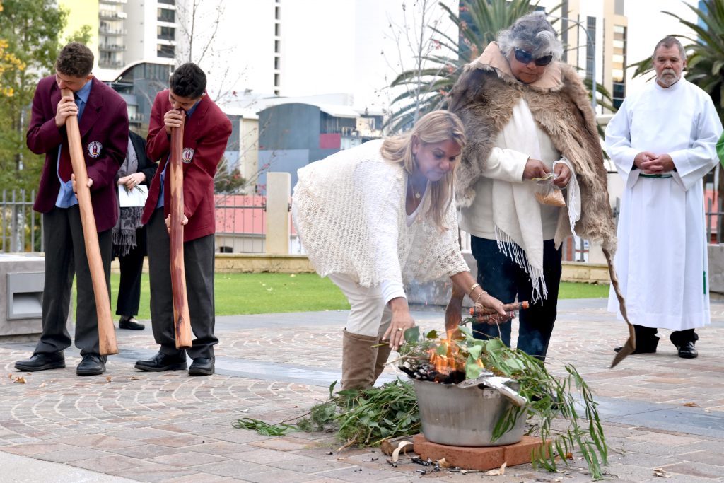 Aboriginal elder Therese Walley and her daughter Rose add more leaves to the fire as part of the smoking ceremony for the end of NAIDOC Week Mass. Aboriginal students from Lumen Christi College Brandon and Thairon Jansen were playing the digeridoo in the background. Photo: Daniele Foti-Cuzzola.