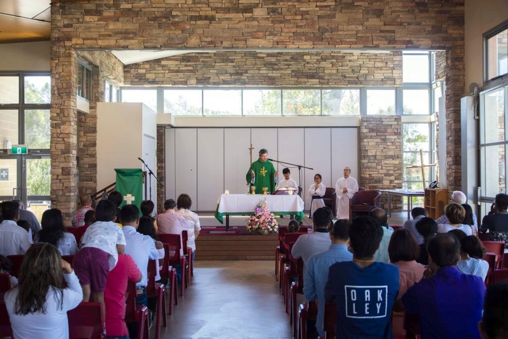 Father Dat Vuong, Yangebup Parish Priest, consecrates the Holy Eucharist in the assembly hall of Hammond Park Catholic Primary School. Photo: Matthew Lau.