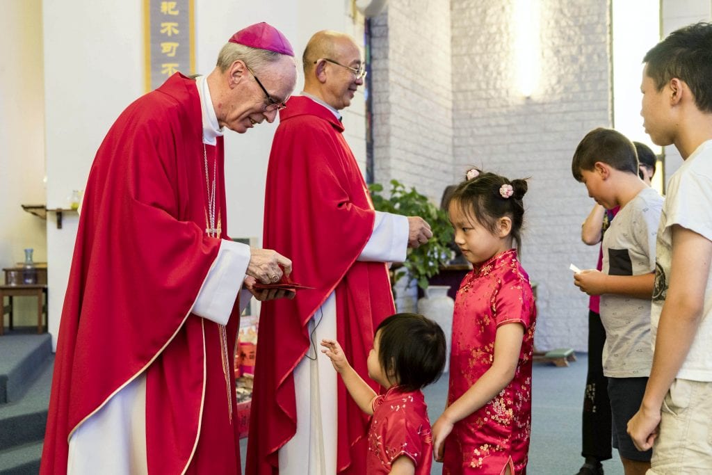 Bishop Donald Sproxton and Father Patrick Lim hand out “hong bao” red packets to the children of the congregation on 10 February 2019. Photo: Matthew Lau.