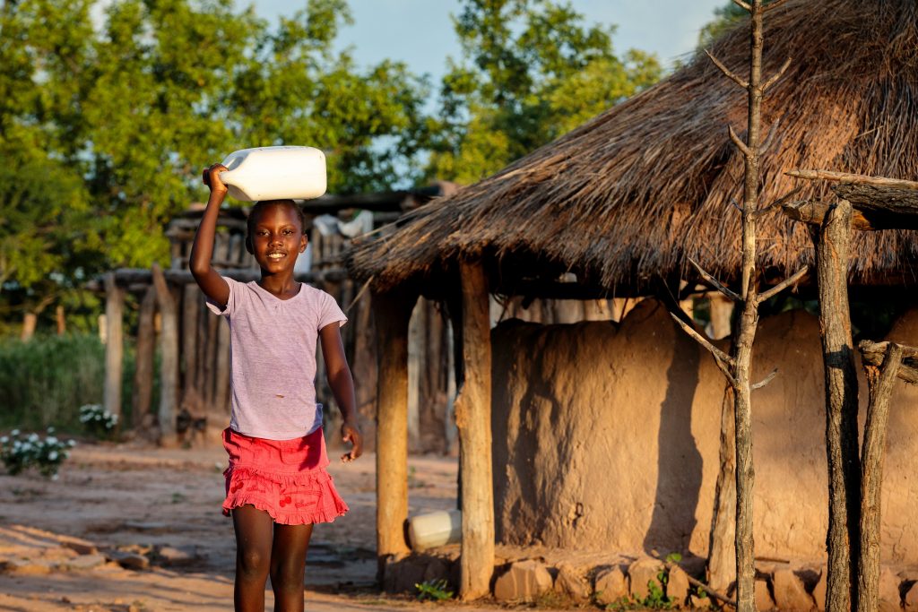 Thandolwayo outside of her home holding a 5 litre water container. Photo: Richard Wainwright/Caritas Australia.