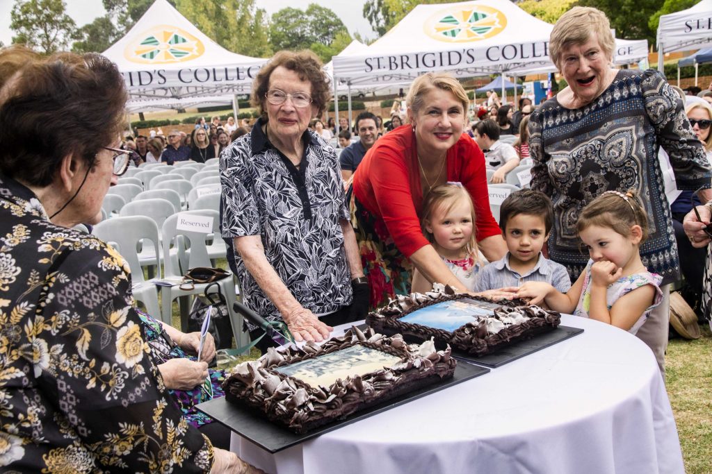 Some of the past and present students of St Brigid’s College cutting the anniversary cake, with Principal Carmen Cox (red top) assisting the younger ones on 31 March. Photo: Amanda Murthy.
