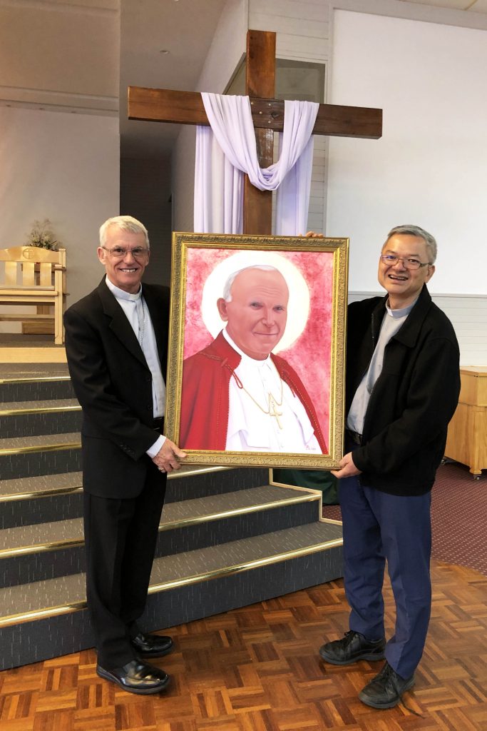 Archbishop Timothy Costelloe SDB pictured with Fr Vinh Dong and the portrait of Saint John Paul II. Photo: Supplied. 