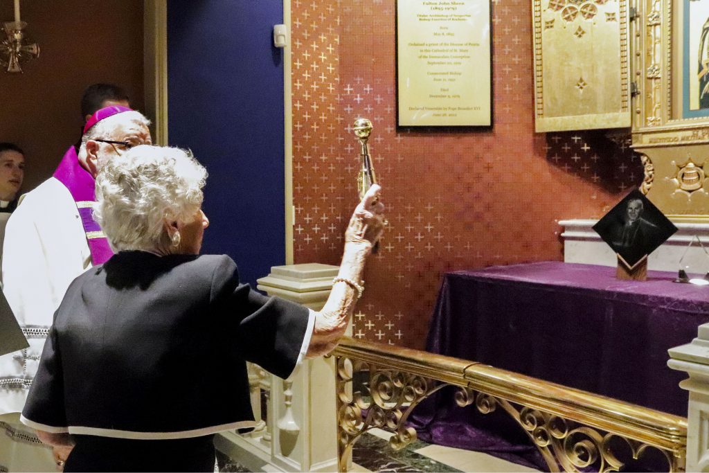 Bishop Daniel R Jenky of Peoria Ill, looks on as Joan Sheen Cunningham, niece of the late Archbishop Fulton J Sheen, sprinkles holy water on the new tomb bearing the remains of her uncle at St Mary's Cathedral in Peoria on 27 June 2019. Archbishop Sheen's remains were transferred from St Patrick's Cathedral in New York City to the Peoria cathedral. Photo: Jennifer Willems/The Catholic Post.