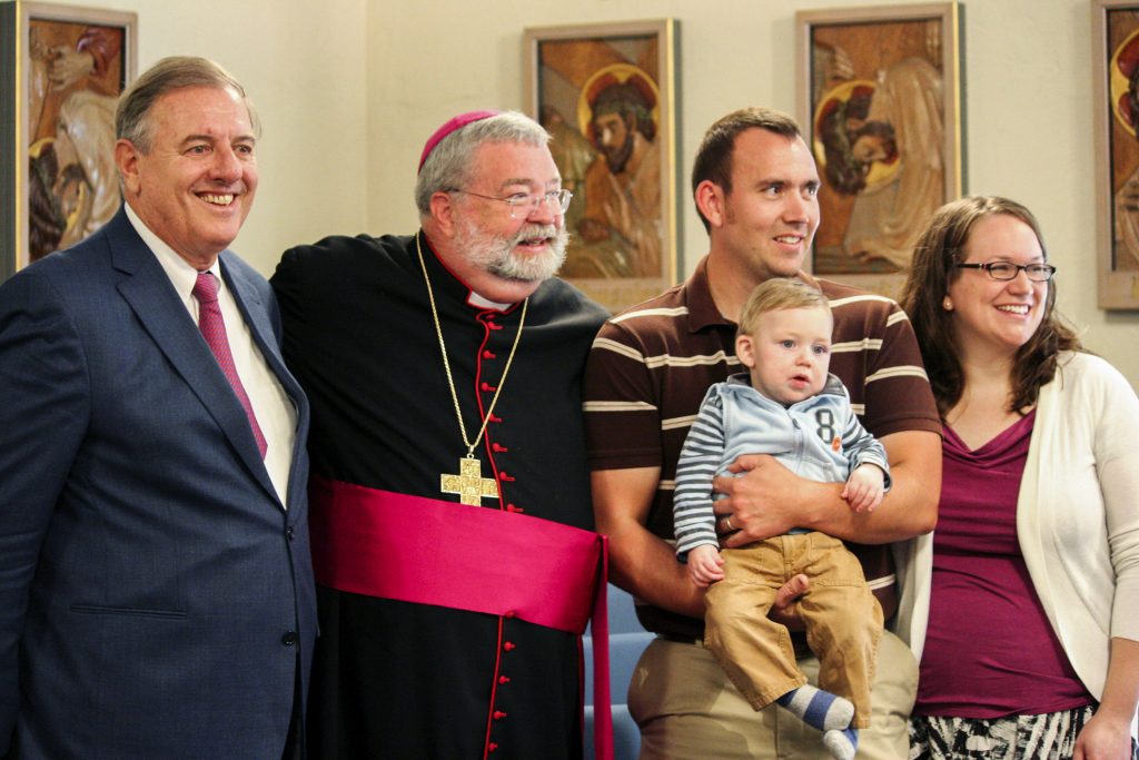 James Fulton Engstrom is held by his parents, Travis and Bonnie Engstrom, on 7 September 2011 at the Spalding Pastoral Center in Peoria Ill as a tribunal began investigating the boy's miraculous healing through the intercession of Archbishop Fulton J Sheen. With them are Andrea Ambrosi, postulator of Archbishop Sheen's sainthood cause, and Peoria Bishop Daniel R Jenky. Photo: Jennifer Willems/The Catholic Post.