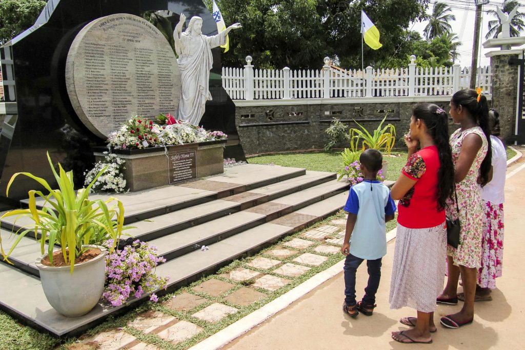 Parishoners of St Sebastian's Church reflect in front of a memorial that lists the names of the martyrs of the Easter Attacks. Photo: Bartek Zytkowiak/Aid to the Church in Need.