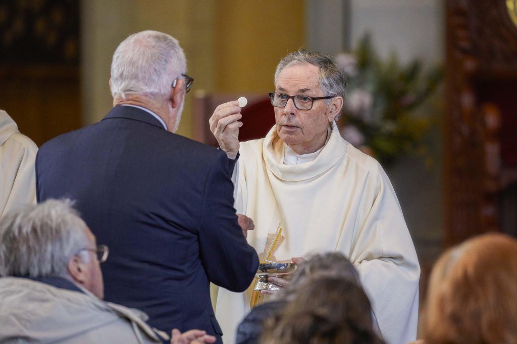 Father Brian McKenna distributes Holy Communion to a receiver. Photo: Ron Tan.