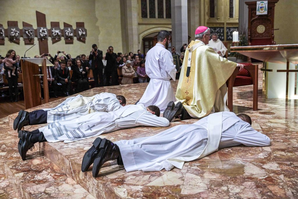 Father’s Liam Ryan, Mark Rucci and Matteo Verdi prostrate during their Ordination Mass on Friday 16 August at the St Mary’s Cathedral. Photo: Ron Tan.