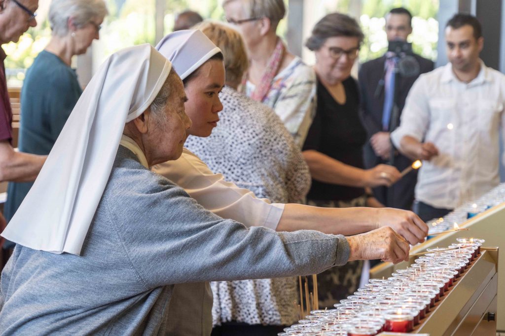Religious Sisters light a candle as part of the Interfaith Prayer Service. Photo: Josh Low.